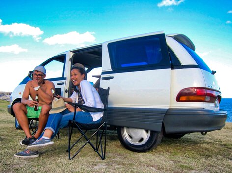 Two people drinking and having fun at the beach after hiring a campervan