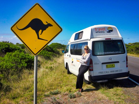 Photo of a woman next to a campervan on the side of the road in Australia next to a kangaroo sign