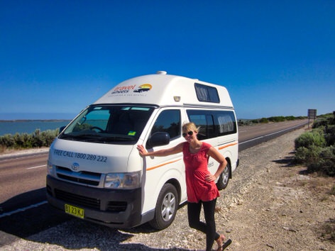 Photo of lovely woman standing by the front of a used Toyota Hiace 3 person campervans for sale from Travelwheels campervans