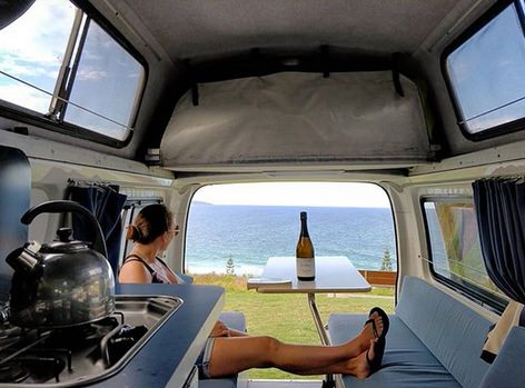 Lovely woman looking outside to the sea drinking wine in Toyota Hiace Campervan