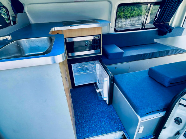 Ex-rental Toyota hiace campervans for sale in Sydney - Photo showing the practical open plan kitchen with sink, worktop space, microwave and 55L two way fridge